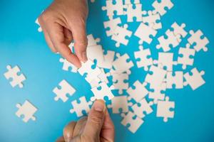 Close up hand holding and playing jigsaw game incomplete. White part of jigsaw puzzle pieces on blue background. concepts of problem solving, business, teamwork. photo