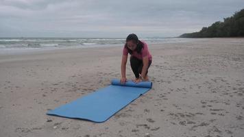 kvinna händer hopfällbar blå yoga matta efter arbetssätt ut på de strand. asiatisk kvinna praktiserande yoga på de stranden. video