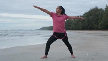 Asian woman practicing yoga at seashore. Young beautiful woman stretching and doing yoga outdoors on blue yoga mat on beach. relaxing in nature video
