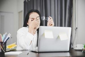 Young business woman person sleepy and has frustration eye problems with cephalalgia disease from using laptop computer on her office desk. Stressed female employee tired and exhausted from overwork. photo