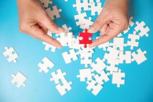 Close up hand holding and playing jigsaw game incomplete. White part of jigsaw puzzle pieces on blue background. concepts of problem solving, business, teamwork. photo