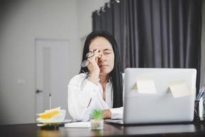 joven mujer de negocios soñolienta y tiene problemas oculares de frustración con la enfermedad de cefalea por usar una computadora portátil en su escritorio de oficina. una empleada estresada cansada y exhausta por el exceso de trabajo.