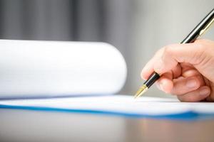 Workplace closeup person professional businesswoman sitting at desk hold pen signing or signature contract paper. Employee woman writing agreement document on paperwork form corporate at work office photo