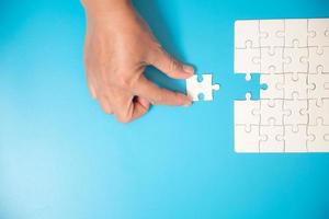 Close up hand holding and playing jigsaw game incomplete. White part of jigsaw puzzle pieces on blue background. concepts of problem solving, business, teamwork. photo