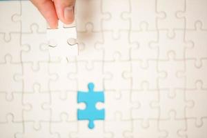 Close up hand holding and playing jigsaw game incomplete. White part of jigsaw puzzle pieces on blue background. concepts of problem solving, business, teamwork. photo