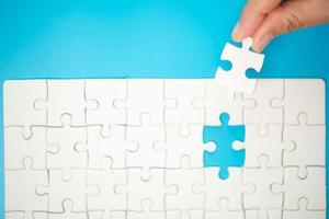 Close up hand holding and playing jigsaw game incomplete. White part of jigsaw puzzle pieces on blue background. concepts of problem solving, business, teamwork. photo