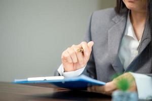 Workplace closeup person professional businesswoman sitting at desk hold pen signing or signature contract paper. Employee woman writing agreement document on paperwork form corporate at work office photo