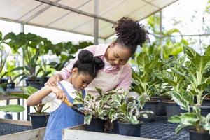 African mother is teaching her daughter to grow ornamental houseplant using trowel to put organics compost in their own nursery garden center