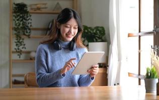 Portrait of smiling happy beautiful asian woman relaxing using technology of tablet while sitting on table.Young creative girl working and typing on keyboard at home.work at home concept photo