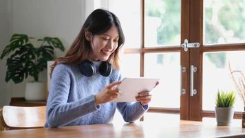Portrait of smiling happy beautiful asian woman relaxing using technology of tablet while sitting on table.Young creative girl working and typing on keyboard at home.work at home concept photo