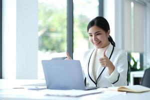 Distant communication. Friendly pretty asian brunette girl, manager, freelancer, sit in the kitchen, talking on video call by laptop with the client or employees, discussing project, smiling photo