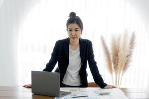 encantadora mujer de negocios asiática con una sonrisa de pie inteligente en la oficina mirando a la cámara. foto