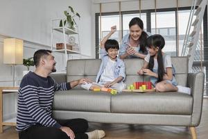 Happy Asian lovely Thai family care, dad, mum, and little children have fun playing with colorful toy blocks together on sofa in white living room, leisure weekend, and domestic wellbeing lifestyle. photo