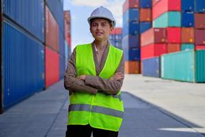 retrato de una trabajadora blanca profesional con uniforme de seguridad y brazos duros cruzados y mira los trabajos de cámara en contenedores logísticos, transporte de carga de importación y exportación, industria del transporte. foto