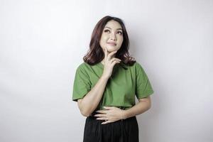 Hermosa mujer asiática hambrienta en camiseta verde sosteniendo su estómago piensa en comida sabrosa aislada sobre fondo blanco foto