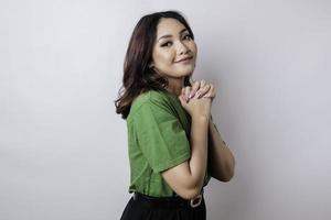 A portrait of Asian woman wearing green t-shirt is praying for success isolated by white background photo