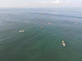 vista aérea de personas surfeando en olas con tablas de surf cuando están de vacaciones en bali, indonesia foto