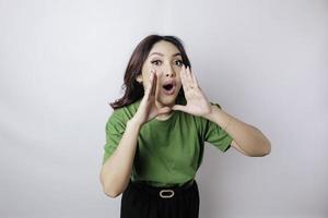 joven mujer hermosa con una camiseta verde gritando y gritando fuerte con una mano en la boca. concepto de comunicación. foto