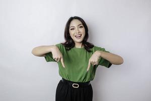 Excited Asian woman wearing green t-shirt pointing at the copy space downside her, isolated by white background photo