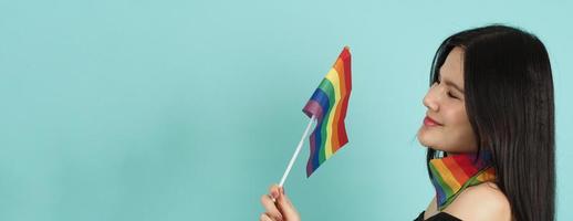 LGBTQ woman holding pride flag standing against a blue green background. photo