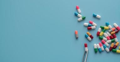 Antibiotic drug selection. Multi-colored capsule pills on blue background. Forceps picks a red-white capsule up from many antibiotic capsule pills. Chance of being selected. Probability sampling. photo