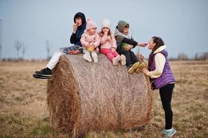 Four kids with mother having fun on haycock at field. photo