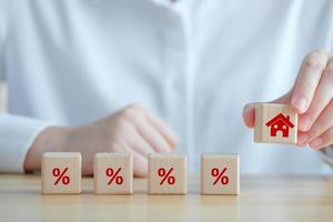 House and property investment and asset management concept. Interest rates, loan mortgage, house tax. Hand holding house icon on wooden block from stack of percentage icon. photo