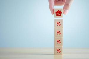 House and property investment and asset management concept. Interest rates, loan mortgage, house tax. Hand holding house icon on wooden block from stack of percentage icon. photo