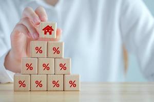 House and property investment and asset management concept. Interest rates, loan mortgage, house tax. Hand holding house icon on wooden block from stack of percentage icon. photo