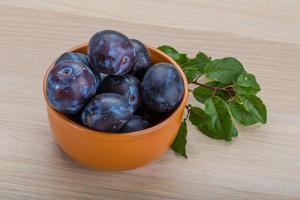 ciruelas frescas en un recipiente sobre fondo de madera foto