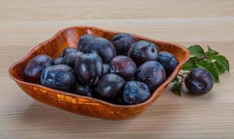 Fresh plums in a bowl on wooden background photo