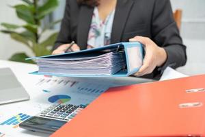 Asian accountant holding binder and working  analyzing financial project accounting with chart graph and laptop in modern office, finance and business concept. photo