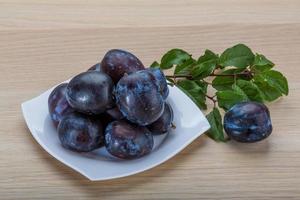 Fresh plums on the plate and wooden background photo