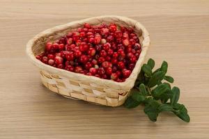 Cowberry in a basket on wooden background photo