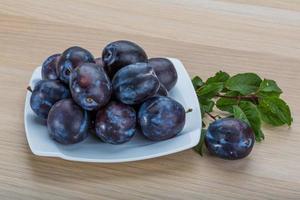 Fresh plums on the plate and wooden background photo