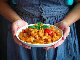 Woman hold a dish of macaroni with tomato sauce in hand photo