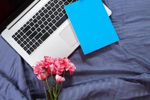 Hands, computer keyboard, bed top view. Workplace background, work at home, notepad and flowers photo