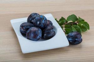 Fresh plums in a bowl on wooden background photo