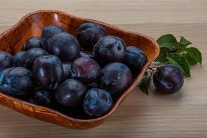 Fresh plums in a bowl on wooden background photo