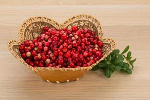 Cowberry in a basket on wooden background photo