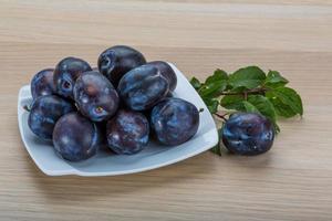 Fresh plums on the plate and wooden background photo