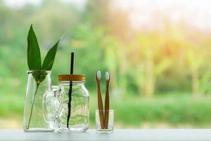 Zero waste use less plastic concept eco green leaf in water glass jar with straw pitcher vase and bamboo toothbrush photo