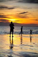 Silhouette of two adults and a child at the coast photo