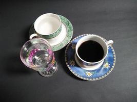 taza de té, taza de café y vidrio transparente con motivos de frutas lleno de agua mineral sobre un fondo negro. foto