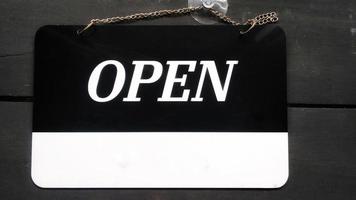 Open signboard black and white color with a symbol that means Shop is open. Hanging on a wooden wall. photo