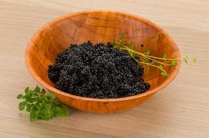 Black caviar in a bowl on wooden background photo