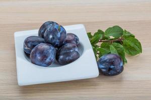 Fresh plums in a bowl on wooden background photo