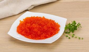Red caviar on the plate and wooden background photo