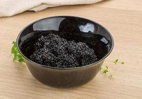 Black caviar in a bowl on wooden background photo