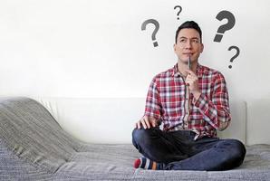 Man on couch contemplating options with questions marks in the background photo